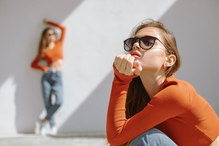 Young woman drinking drink sitting against wall