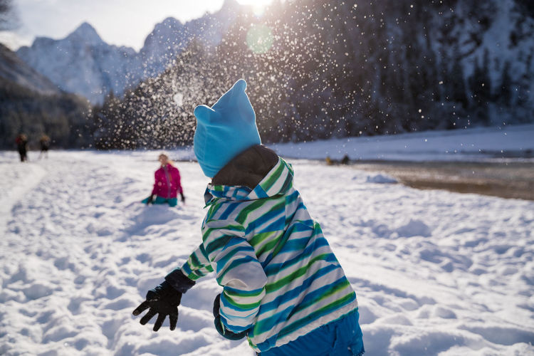 Rear view of boy playing with snow during winter
