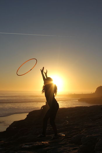 Silhouette girl throwing plastic hoop while standing on beach