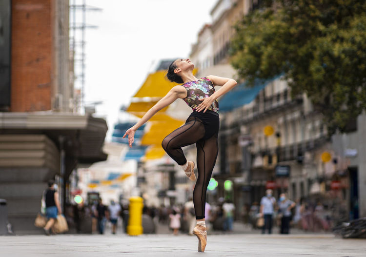 Dancer practicing ballet dancing while standing tiptoe on street in city