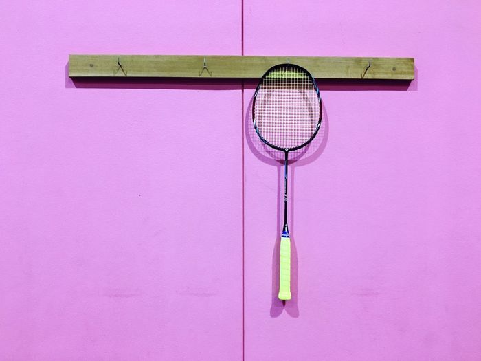 Close-up of badminton racket hanging against pink wall