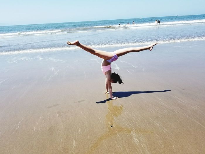 Full length of girl doing handstand at beach during sunny day