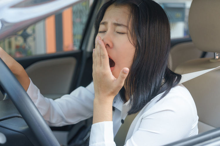 Young woman yawning while driving car