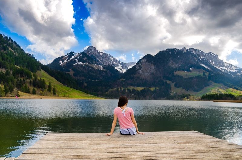 Rear view of girl by lake against cloudy sky