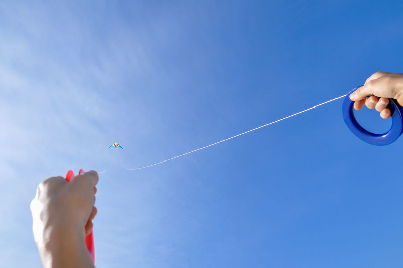 Low angle view of hand holding kite against blue sky
