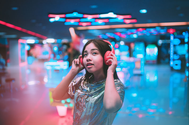 Young woman listening music while standing in illuminated room