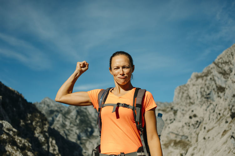 Hiker showing biceps while standing against sky at cares trail in picos de europe national park, asturias, spain