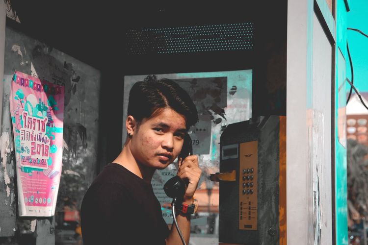 Portrait of young man using pay phone