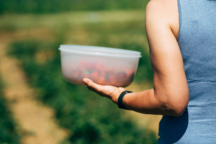 Cropped image of woman holding strawberries in container on field