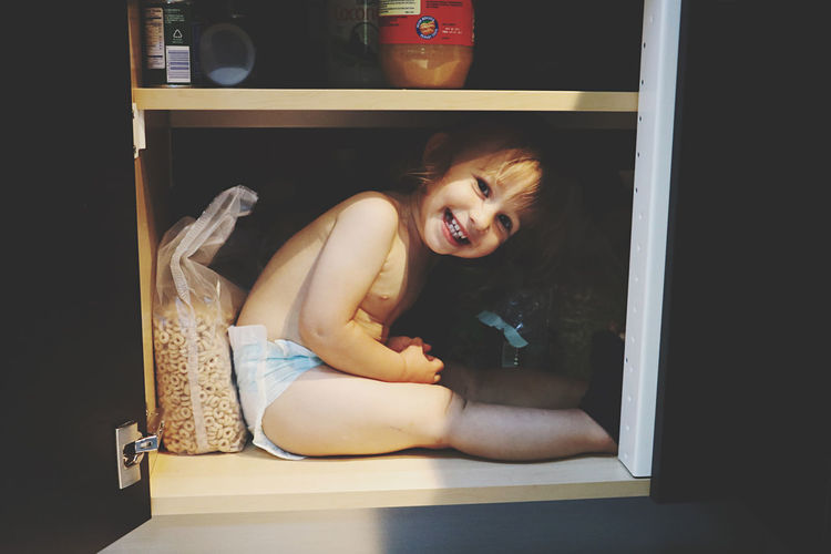 Cute little girl hiding inside kitchen cabinet