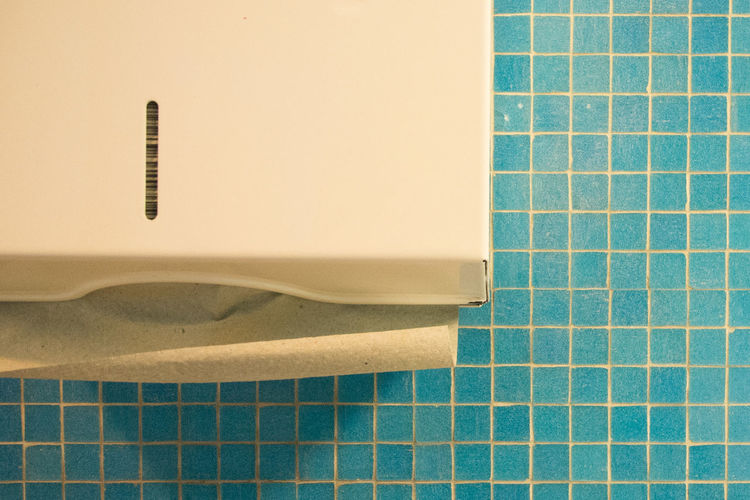 Close-up of tissue dispenser on blue tile wall
