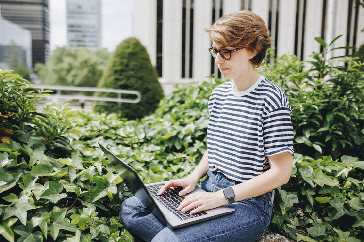 Woman working on laptop sitting amidst plants