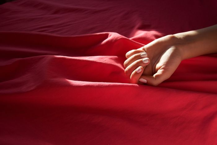 Cropped hand of woman on red satin sheet over bed at home