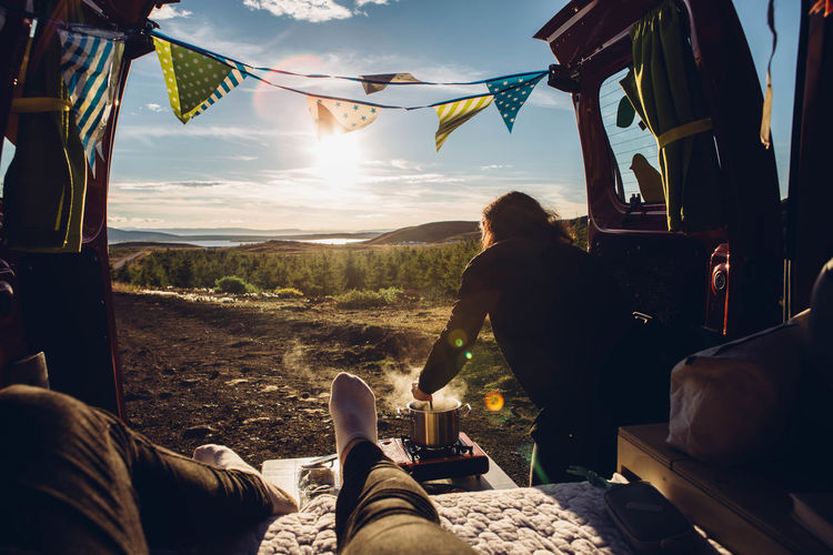 Two people sitting in campervan cooking and looking at view