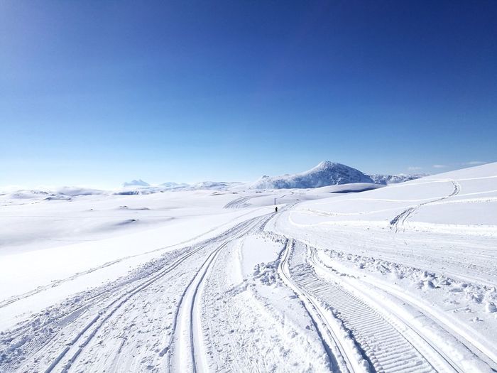 Tire tracks on snow against clear blue sky