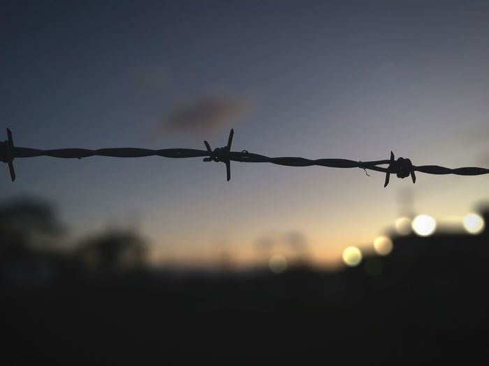 Barbed wire against sky at sunset