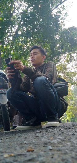 Young man using mobile phone while sitting on tree