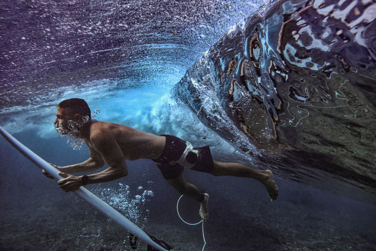 Male surfer diving underwater with surfboard at maldives