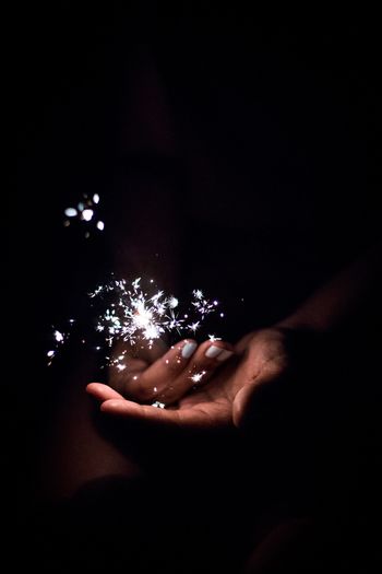 Cropped hand of woman holding burning sparkler at night