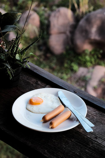 American breakfast with eggs and sausage put on white plate with knife , wood background.