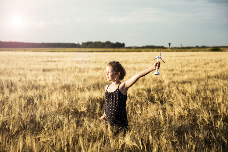 Girl standing in grain field holding miniature wind turbine