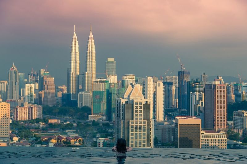 Rear view of woman in marina bay sands swimming pool looking at petronas towers during sunset