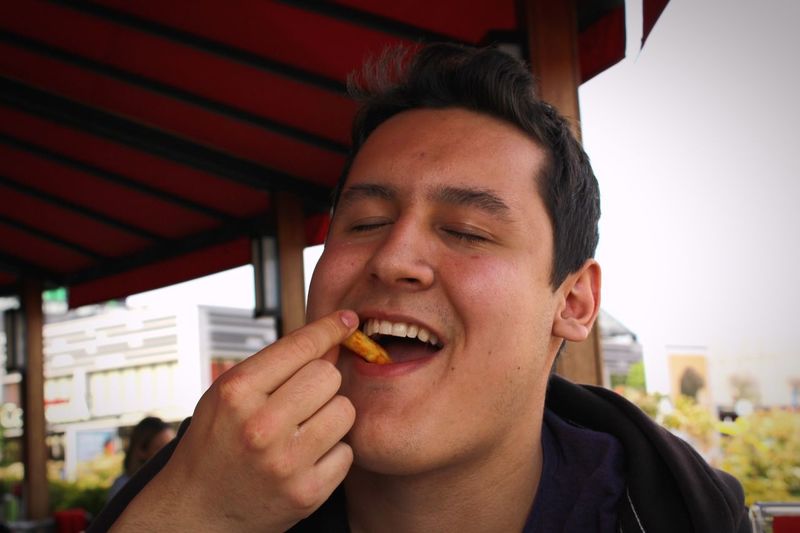 Smiling man with closed eyes eating potato chips at restaurant