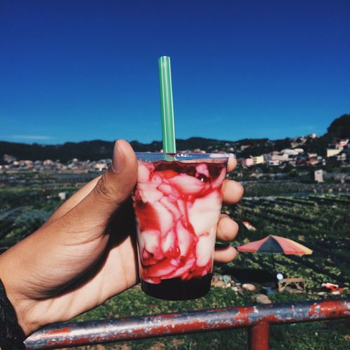 Cropped hands of person holding drink against clear blue sky