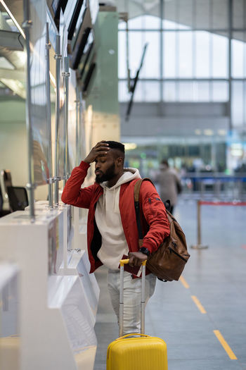 Upset african man standing at check-in counter in airport, being sad about moving away