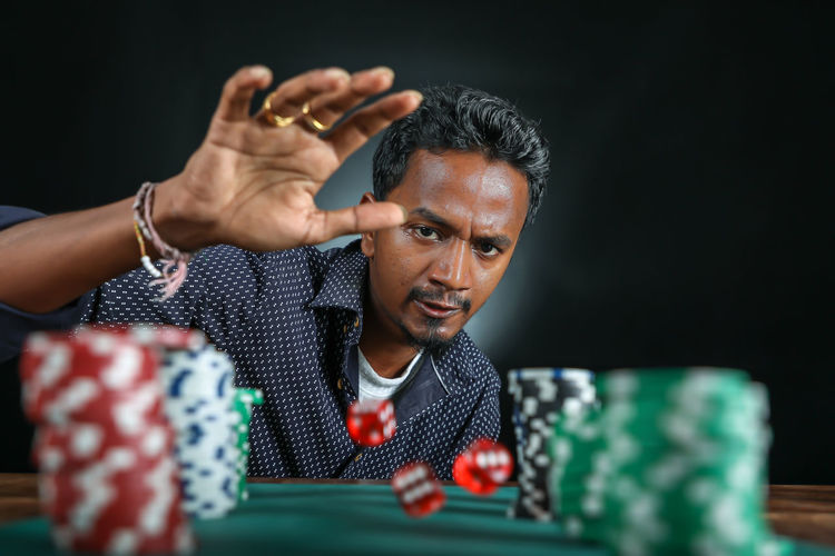 Confident mature man rolling dice at craps table against black background