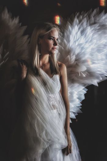 Young woman wearing angel costume looking away while standing indoors