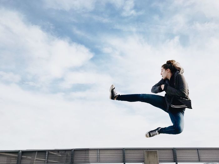 Full length of woman jumping against cloudy sky