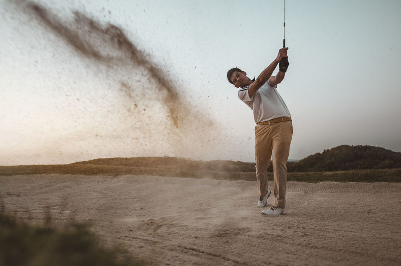 Full length of man playing golf against sky at sunset