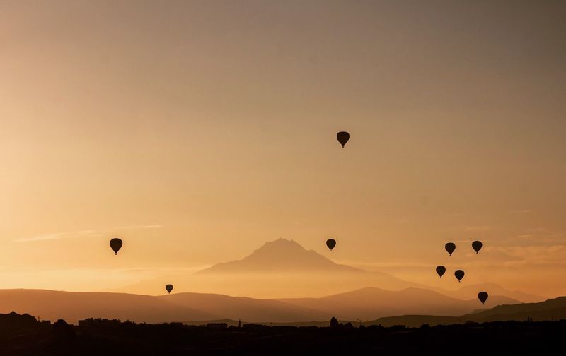 Hot air balloons flying over mountains against sky during sunset