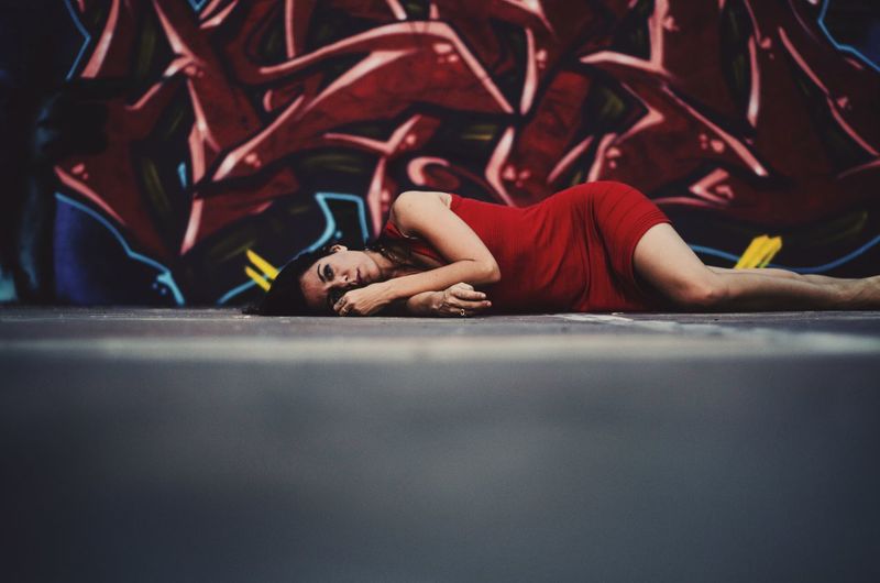 Portrait of woman lying on floor against graffiti wall