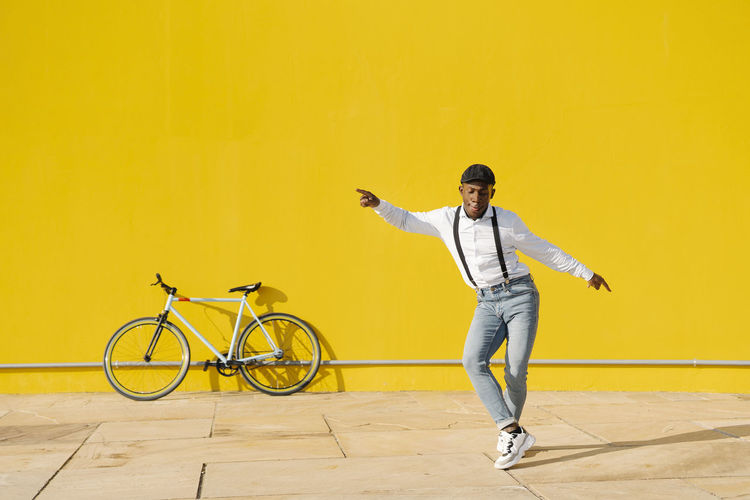 Full length of man jumping against yellow wall