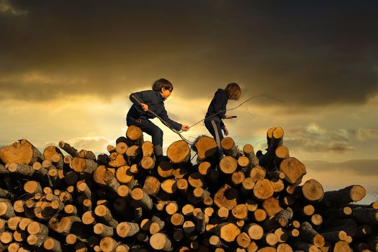 Two kids walking on log against sky during sunset