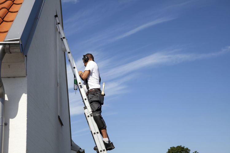 Low angle view of man working on blue sky