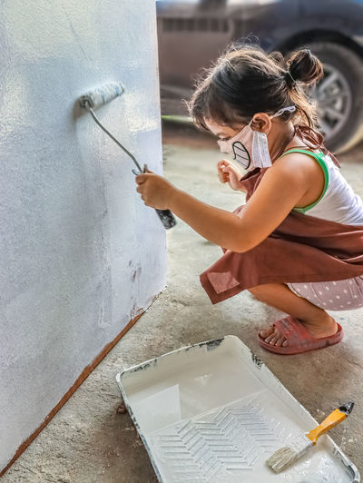 Squatting child holding paint roller against wall