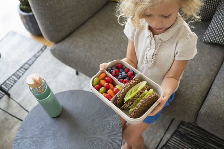Girl holding lunch box with healthy food on sofa at home