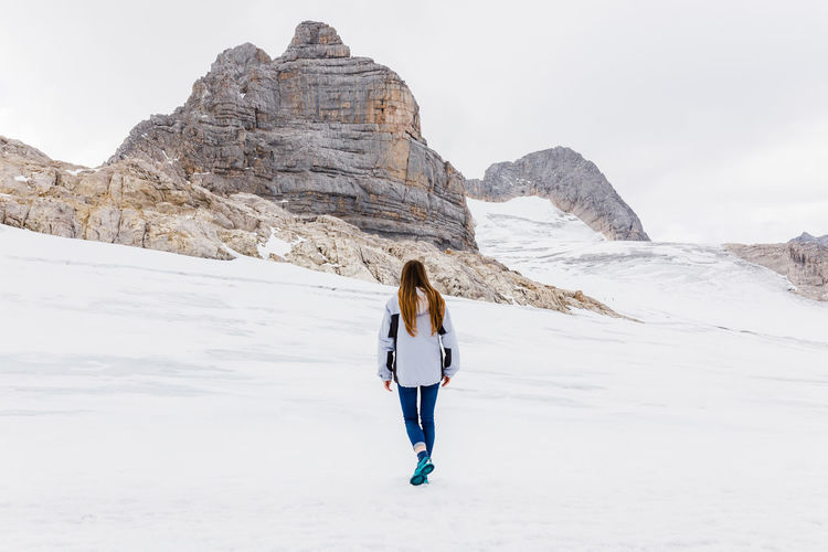 Rear view of woman standing on snowcapped mountain against sky