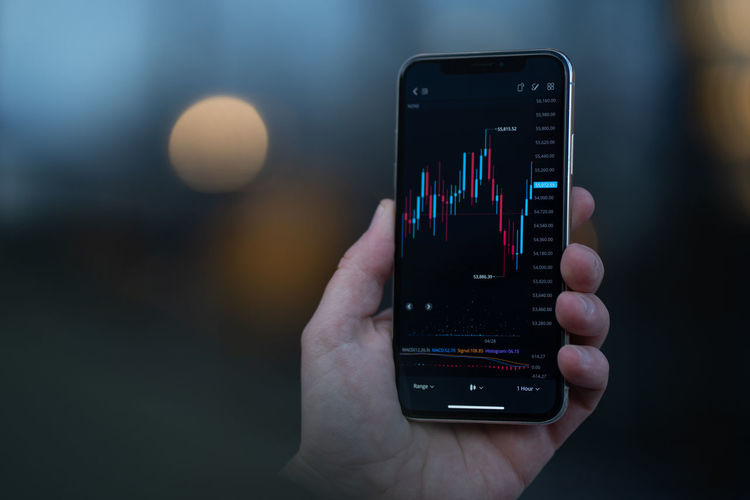 Cropped hand of trader holding mobile phone with graphs on screen