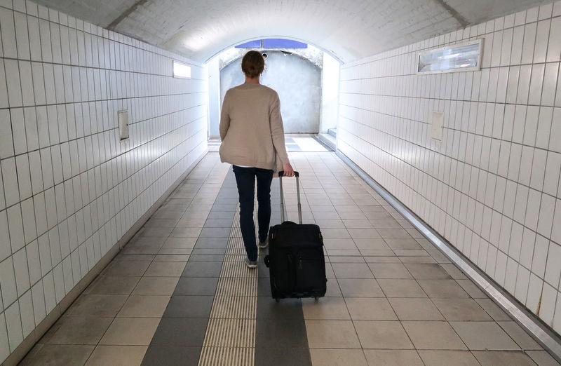 Rear view of young woman with luggage walking in illuminated tunnel
