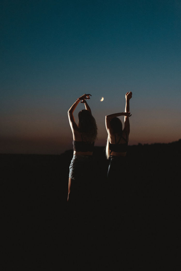 Silhouette women with arms raised against sky during dusk