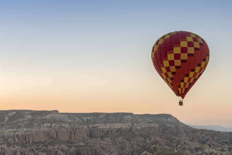 Hot air balloon flying over rock formation against clear sky