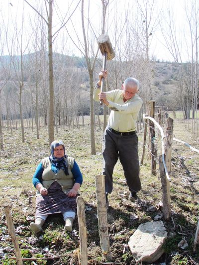 Senior man hammering wooden post by woman sitting on field