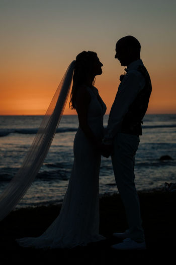 Bride and groom  standing on beach against sky during sunset