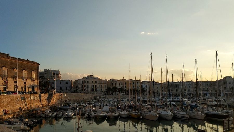 Sailboats moored in harbor against buildings in city during sunset