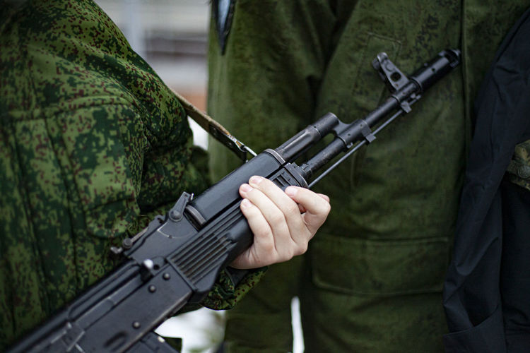 Midsection of army soldiers holding assault rifle while standing with colleague