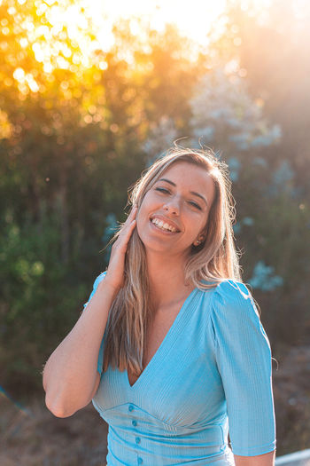 Portrait of smiling young woman standing in forest at sunset